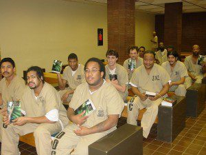 A group of men in prison uniforms sitting on some benches.